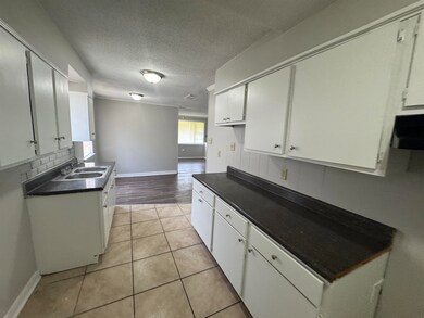 Kitchen with dark countertops, white cabinetry, backsplash, light tile patterned floors, and a textured ceiling
