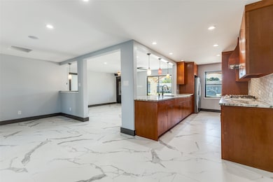 Kitchen with light stone counters, brown cabinetry, pendant lighting, open floor plan, and tasteful backsplash
