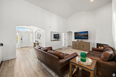 Living room featuring high vaulted ceiling, arched walkways, light wood-type flooring, and a lit fireplace
