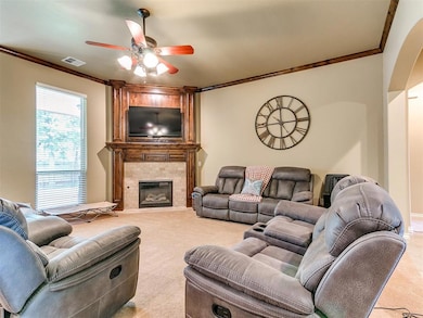 Carpeted living area featuring ornamental molding, a ceiling fan, and a large fireplace