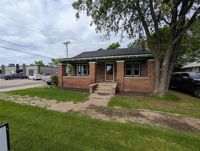 Bungalow-style house featuring brick siding, a front yard, uncovered parking, a chimney, and a shingled roof