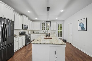 Kitchen with appliances with stainless steel finishes, dark wood-style flooring, white cabinetry, a center island, and recessed lighting