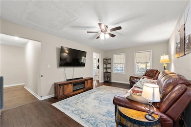Living room featuring dark wood-type flooring, a ceiling fan, and a textured ceiling