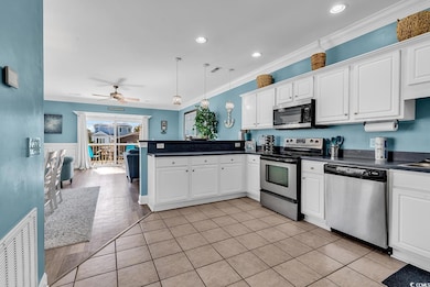 Kitchen featuring appliances with stainless steel finishes, white cabinetry, dark countertops, light tile patterned flooring, and crown molding