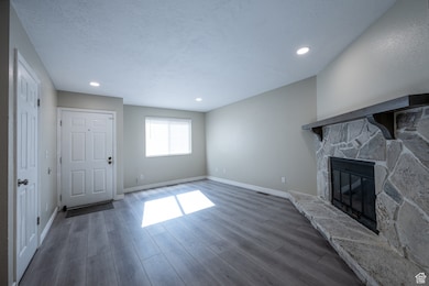 Unfurnished living room featuring a stone fireplace, wood finished floors, recessed lighting, and a textured ceiling