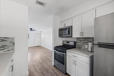 Kitchen featuring decorative backsplash, stainless steel appliances, white cabinets, and dark wood-type flooring