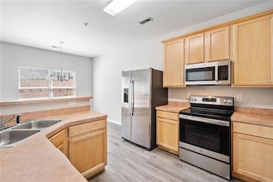 Kitchen featuring appliances with stainless steel finishes, light brown cabinetry, a sink, a chandelier, and light countertops