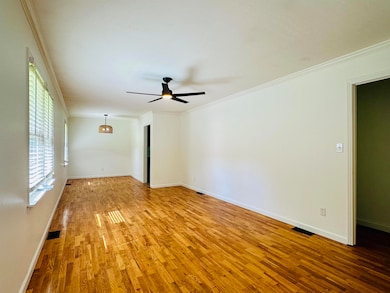 Empty room with light wood-style floors, ceiling fan, ornamental molding, and baseboards