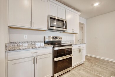 Kitchen featuring stainless steel appliances, white cabinetry, light wood-style floors, and light stone countertops