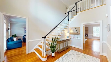 Spacious foyer with soaring ceilings, crown molding, and hardwood flooring. Abundant natural light enhances the elegant architectural details.