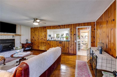 Living area with a textured ceiling, a brick fireplace, a ceiling fan, wooden walls, and wood finished floors