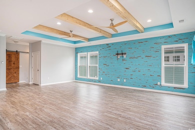 Spare room featuring ceiling fan, wallpapered walls, wood finished floors, a barn door, and beamed ceiling