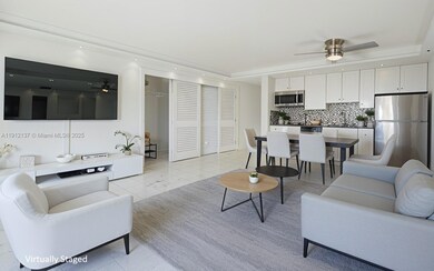 Sunlight fills the open space through floor-to-ceiling sliding doors, highlighting the gleaming floors and mirrored accent wall that enhances depth and natural light. The modern layout seamlessly connects to a private balcony with lush palm views, creating a serene indoor-outdoor flow. Clean lines, recessed lighting, and refined finishes make this residence the perfect blend of luxury and tranquility