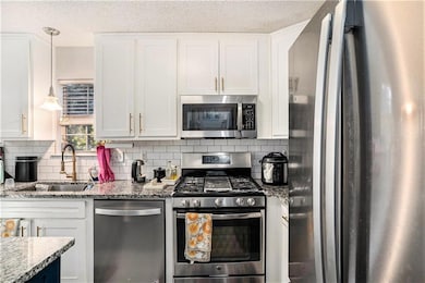 Kitchen with stainless steel appliances, white cabinetry, hanging light fixtures, and a textured ceiling