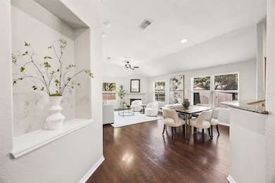 The heart of the home shines with natural light, rich wood flooring, and a spacious open-concept layout perfect for entertaining or relaxing. Large windows frame the backyard, while the dining area flows seamlessly into the living room and kitchen.