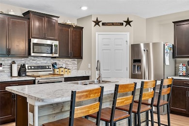 Kitchen with dark brown cabinetry, light countertops, appliances with stainless steel finishes, a kitchen bar, and a textured ceiling