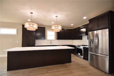 Kitchen with stainless steel appliances, decorative backsplash, a kitchen island, light wood-style flooring, and recessed lighting