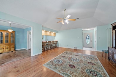 Living room with a ceiling fan, wood finished floors, lofted ceiling, baseboards, and bar area