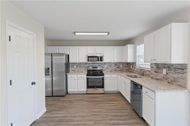 Kitchen featuring appliances with stainless steel finishes, white cabinetry, decorative backsplash, light wood-type flooring, and light stone counters
