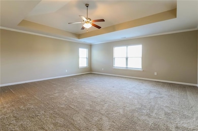 Empty room with a tray ceiling, ornamental molding, light colored carpet, and ceiling fan
