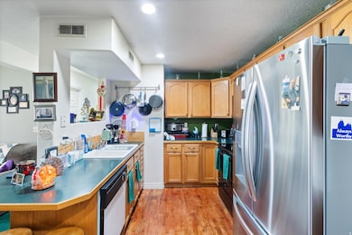 Kitchen featuring stainless steel refrigerator with ice dispenser, light wood finished floors, a textured ceiling, black range oven, and dishwasher