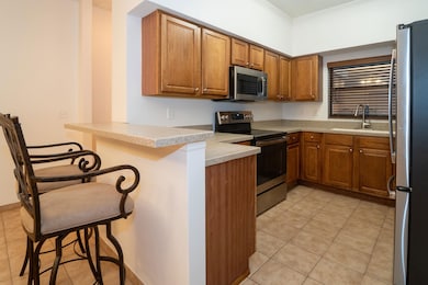 Kitchen featuring brown cabinetry, a breakfast bar, light tile patterned flooring, appliances with stainless steel finishes, and a peninsula