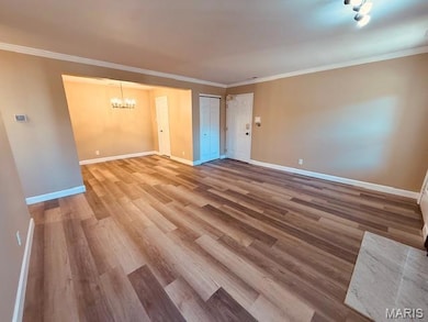 Unfurnished living room with ornamental molding, a chandelier, and light wood finished floors