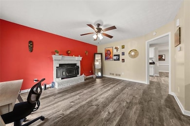 Living area with wood finished floors, ceiling fan, a fireplace, an accent wall, and baseboards