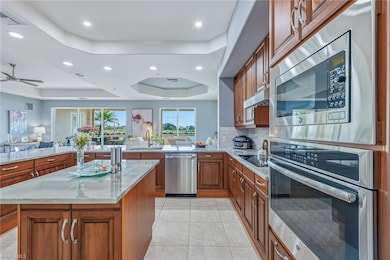 Kitchen with brown cabinets, appliances with stainless steel finishes, a raised ceiling, light tile patterned floors, and light stone countertops
