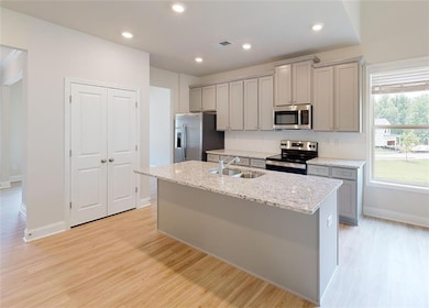 Kitchen with stainless steel appliances, an island with sink, sink, light wood-type flooring, and gray cabinetry