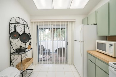 Kitchen with green cabinetry, light countertops, white microwave, and light tile patterned flooring