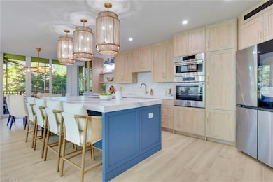 Kitchen with light brown cabinetry, a chandelier, stainless steel appliances, open shelves, and tasteful backsplash