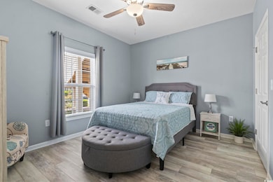 Bedroom with light wood-type flooring, multiple windows, and ceiling fan