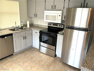 Kitchen featuring stainless steel appliances, light tile patterned flooring, light stone countertops, and gray cabinetry