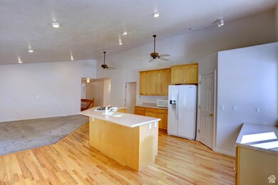 Kitchen with white appliances, light countertops, open floor plan, a center island with sink, and light wood finished floors