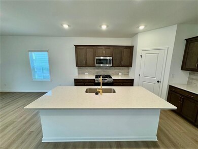Kitchen featuring stainless steel appliances, light wood-type flooring, decorative backsplash, dark brown cabinets, and a kitchen island with sink