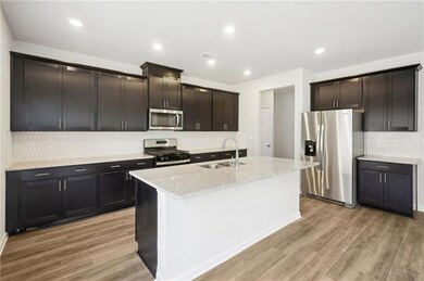 Kitchen featuring appliances with stainless steel finishes, light wood-style flooring, decorative backsplash, a center island with sink, and recessed lighting
