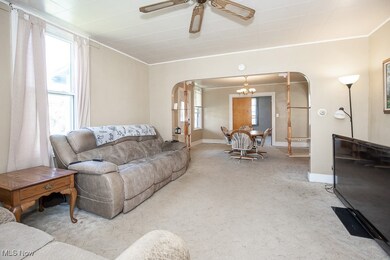 Living room featuring arched walkways, carpet floors, a ceiling fan, ornamental molding, and a chandelier