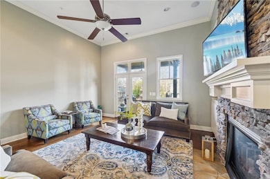 Living area featuring a stone fireplace, a ceiling fan, ornamental molding, and wood finished floors