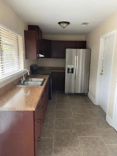 Kitchen with fridge, stainless steel range, dark tile patterned floors, dark brown cabinets, and a textured ceiling