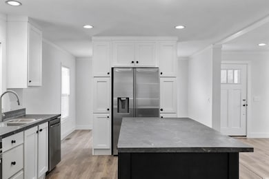 Kitchen featuring dark countertops, stainless steel appliances, crown molding, white cabinets, and light wood finished floors