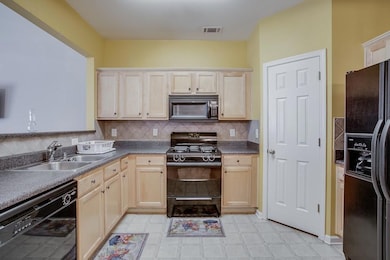 Kitchen with black appliances, light floors, light brown cabinets, and backsplash
