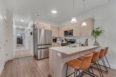 Kitchen with appliances with stainless steel finishes, light brown cabinets, decorative light fixtures, a kitchen bar, and a peninsula