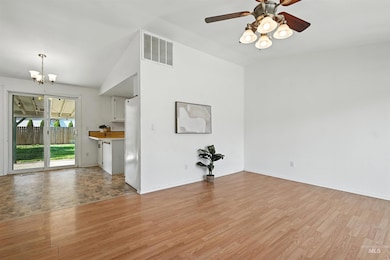 Unfurnished living room featuring a chandelier, light wood-style flooring, ceiling fan, and lofted ceiling
