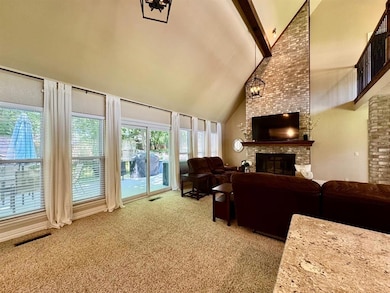 Living area with high vaulted ceiling, beam ceiling, light colored carpet, a brick fireplace, and a chandelier