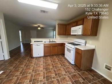 Kitchen with white appliances, light countertops, brown cabinetry, a peninsula, and a ceiling fan