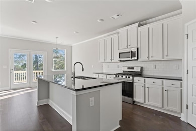 Kitchen featuring a sink, appliances with stainless steel finishes, a kitchen island with sink, visible vents, and ornamental molding