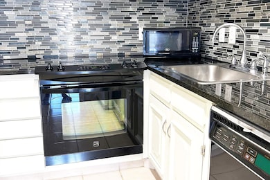 Kitchen featuring tasteful backsplash, black appliances, and white cabinets