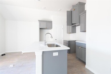 Kitchen with gray cabinetry, a sink, a kitchen island with sink, tasteful backsplash, and light wood finished floors