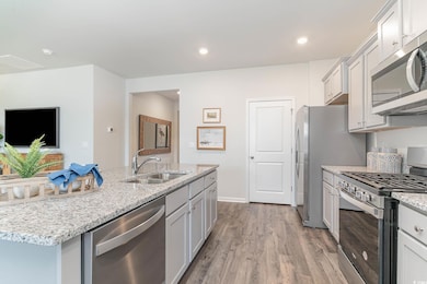 Kitchen with sink, light hardwood / wood-style floors, stainless steel appliances, light stone countertops, and a center island with sink